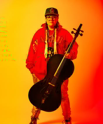A performer stands with a large stringed instrument in front of a yellow-orange gradient.